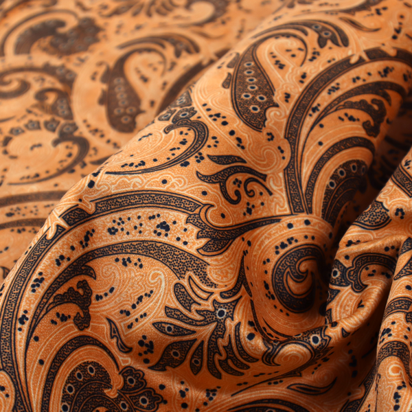 A complex textile design featuring an all-over paisley and scroll pattern in solid black over a warm copper-orange background. The motifs are highly stylized with a mixture of dotted textures, fine line work, and bold curves that resemble ocean waves or flowing vines. The high-contrast colour palette gives the fabric a sophisticated, bohemian-luxe appearance.