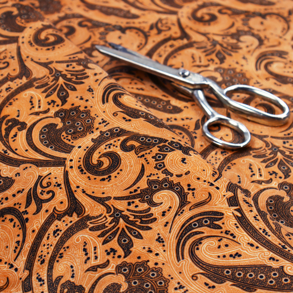 A complex textile design featuring an all-over paisley and scroll pattern in solid black over a warm copper-orange background. The motifs are highly stylized with a mixture of dotted textures, fine line work, and bold curves that resemble ocean waves or flowing vines. The high-contrast colour palette gives the fabric a sophisticated, bohemian-luxe appearance.