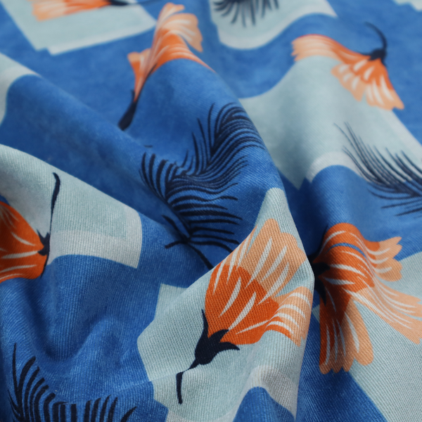 Modern tropical fabric featuring a vibrant cobalt blue background with scattered orange fan-shaped flowers, dark navy palm fronds, and pale blue geometric square overlays.