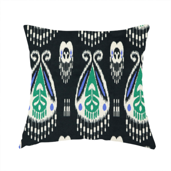 The fabric used to create this handmade cushion is a dark textile featuring rows of floating, feathered ikat medallions. The design glows with emerald green and bright sapphire blue against a deep obsidian background, accented by crisp white geometric tassels and swirling crown-like scrollwork.