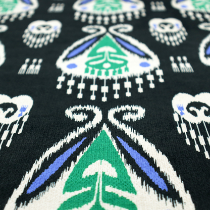 A dark textile featuring rows of floating, feathered ikat medallions. The design glows with emerald green and bright sapphire blue against a deep obsidian background, accented by crisp white geometric tassels and swirling crown-like scrollwork.