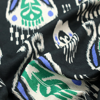A dark textile featuring rows of floating, feathered ikat medallions. The design glows with emerald green and bright sapphire blue against a deep obsidian background, accented by crisp white geometric tassels and swirling crown-like scrollwork.