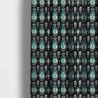 The fabric used to create these made-to-measure curtains is a dark textile featuring rows of floating, feathered ikat medallions. The design glows with emerald green and bright sapphire blue against a deep obsidian background, accented by crisp white geometric tassels and swirling crown-like scrollwork.