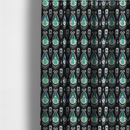 The fabric used to create these made-to-measure curtains is a dark textile featuring rows of floating, feathered ikat medallions. The design glows with emerald green and bright sapphire blue against a deep obsidian background, accented by crisp white geometric tassels and swirling crown-like scrollwork.
