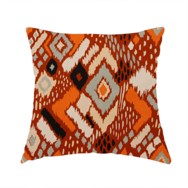 The fabric used to create this handmade cushion is a bohemian ikat fabric featuring a dense diamond pattern in burnt orange, cream, and charcoal black with distressed, hand-stamped textures.