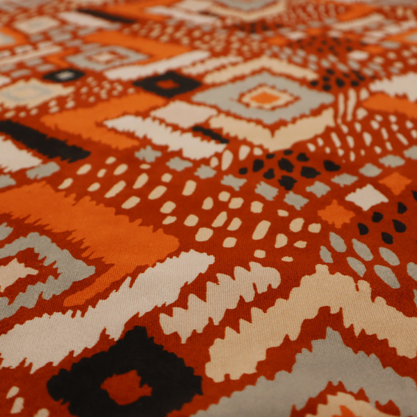 Bohemian ikat fabric featuring a dense diamond pattern in burnt orange, cream, and charcoal black with distressed, hand-stamped textures.