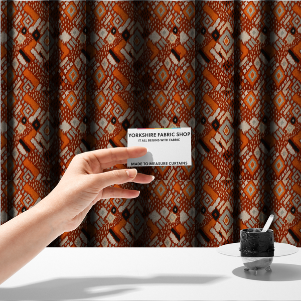 The fabric used to create these made-to-measure curtains is a bohemian ikat fabric featuring a dense diamond pattern in burnt orange, cream, and charcoal black with distressed, hand-stamped textures.
