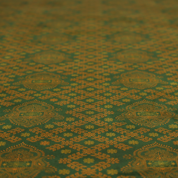 A repeating, decorative fabric pattern featuring ornate, gold-toned paisley motifs centred on a deep forest green background. The design is structured around a subtle lattice of small, delicate floral sprigs, creating a traditional, block-printed aesthetic with a slightly weathered, vintage texture.