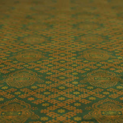A repeating, decorative fabric pattern featuring ornate, gold-toned paisley motifs centred on a deep forest green background. The design is structured around a subtle lattice of small, delicate floral sprigs, creating a traditional, block-printed aesthetic with a slightly weathered, vintage texture.
