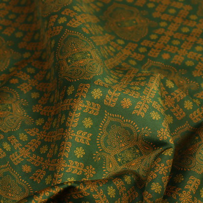 A repeating, decorative fabric pattern featuring ornate, gold-toned paisley motifs centred on a deep forest green background. The design is structured around a subtle lattice of small, delicate floral sprigs, creating a traditional, block-printed aesthetic with a slightly weathered, vintage texture.