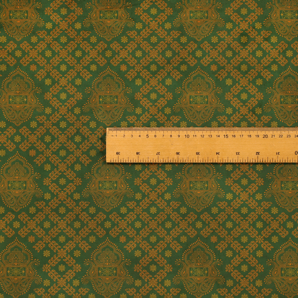 A repeating, decorative fabric pattern featuring ornate, gold-toned paisley motifs centred on a deep forest green background. The design is structured around a subtle lattice of small, delicate floral sprigs, creating a traditional, block-printed aesthetic with a slightly weathered, vintage texture.