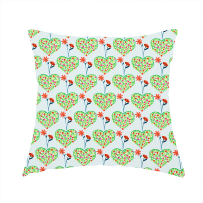 The fabric used to create this handmade cushion is a repeating pattern on a light blue-grey background. The pattern consists of rows of heart shapes made of green vines and small pink and red flowers. Each heart is topped with a red flower on a thin blue stem and flanked by another red flower on its own blue stem. These floral elements repeat across the entire fabric.