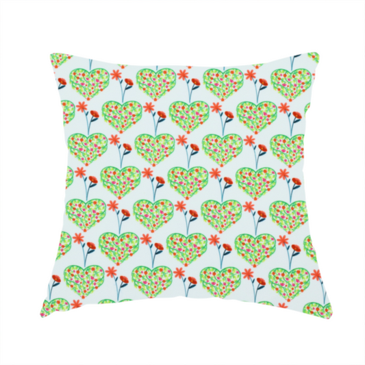 The fabric used to create this handmade cushion is a repeating pattern on a light blue-grey background. The pattern consists of rows of heart shapes made of green vines and small pink and red flowers. Each heart is topped with a red flower on a thin blue stem and flanked by another red flower on its own blue stem. These floral elements repeat across the entire fabric.