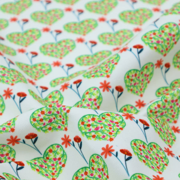 This fabric shows a repeating pattern on a light blue-grey background. The pattern consists of rows of heart shapes made of green vines and small pink and red flowers. Each heart is topped with a red flower on a thin blue stem and flanked by another red flower on its own blue stem. These floral elements repeat across the entire fabric.