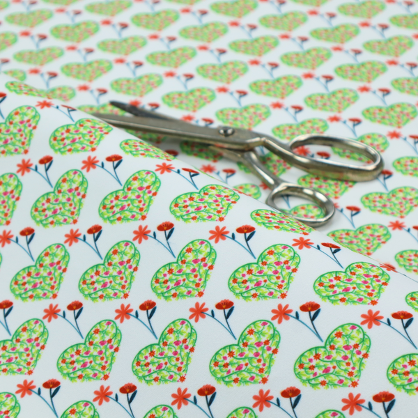 This fabric shows a repeating pattern on a light blue-grey background. The pattern consists of rows of heart shapes made of green vines and small pink and red flowers. Each heart is topped with a red flower on a thin blue stem and flanked by another red flower on its own blue stem. These floral elements repeat across the entire fabric.