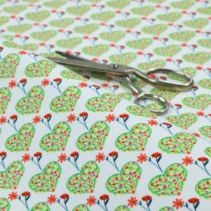 This fabric shows a repeating pattern on a light blue-grey background. The pattern consists of rows of heart shapes made of green vines and small pink and red flowers. Each heart is topped with a red flower on a thin blue stem and flanked by another red flower on its own blue stem. These floral elements repeat across the entire fabric.