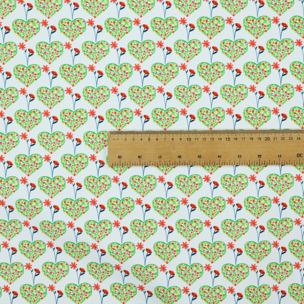 This fabric shows a repeating pattern on a light blue-grey background. The pattern consists of rows of heart shapes made of green vines and small pink and red flowers. Each heart is topped with a red flower on a thin blue stem and flanked by another red flower on its own blue stem. These floral elements repeat across the entire fabric.