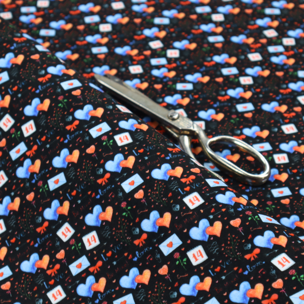 This black fabric features a dense, romantic Valentine’s Day theme with a repeating pattern of watercolour-style motifs. The design includes blue and red hearts, small sealed envelopes, red bows, and calendar pages marked with the number "14". 