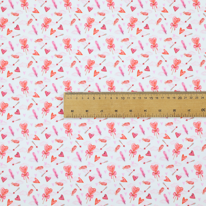 This white fabric features a light, whimsical Valentine’s Day pattern with watercolour elements scattered across a pale background. The design includes pink heart-shaped balloons tied with bows, soft pink feathers, and various small arrows and hearts. Faint, dreamy cloud-like textures in pink and blue are visible in the background, adding to the soft, airy aesthetic.