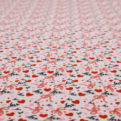 This light pink fabric features a dense, repeating Valentine’s Day pattern with a vintage, romantic aesthetic. The design is composed of small red hearts and larger pink hearts, interspersed with delicate red ribbon bows and the word "love" written in a dark, flowing cursive script. Tiny red dots are scattered throughout the background, creating a textured, confetti-like effect across the entire print.