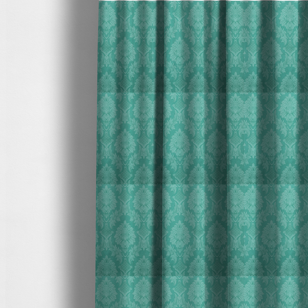 The fabric used to create these made-to-measure curtains is a vibrant teal damask fabric featuring a large-scale, repeating floral and acanthus leaf pattern in a tonal, monochromatic seafoam green colourway.