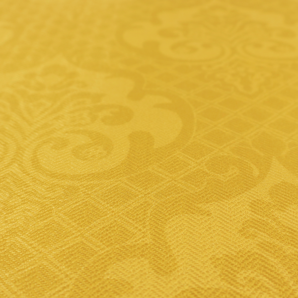A vibrant yellow damask fabric featuring a tonal, monochrome design. Ornate, stylized floral medallions and acanthus leaves are woven in a slightly lighter shade of yellow, creating a subtle shimmer. The pattern is set against a background of a fine diagonal lattice grid, with a visible woven texture throughout the material.
