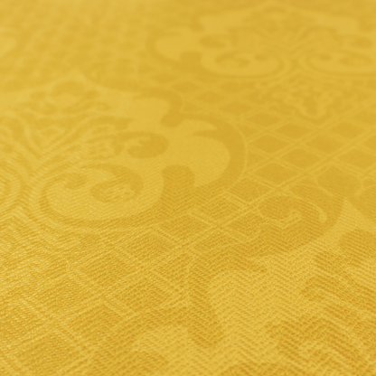 A vibrant yellow damask fabric featuring a tonal, monochrome design. Ornate, stylized floral medallions and acanthus leaves are woven in a slightly lighter shade of yellow, creating a subtle shimmer. The pattern is set against a background of a fine diagonal lattice grid, with a visible woven texture throughout the material.