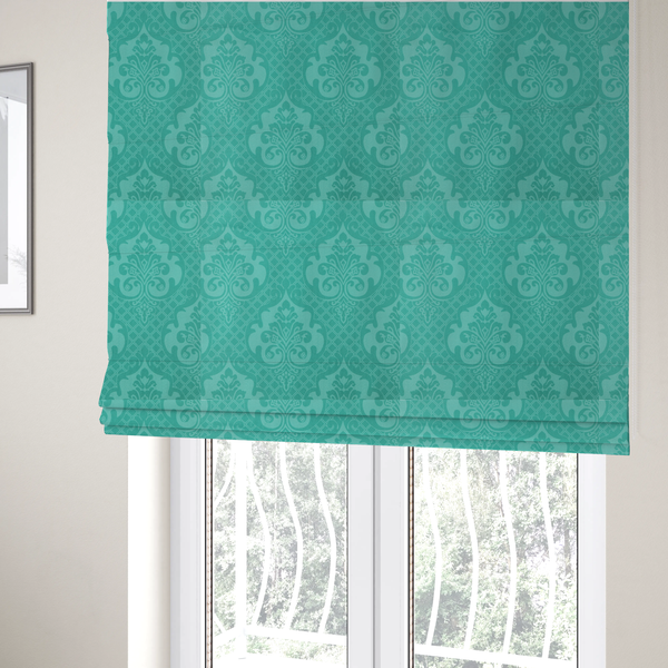 The fabric used to create these Roman blinds has a design that features large, ornate floral medallions and scrolling acanthus leaves in a bright turquoise shade, set against a slightly lighter mint green background. A fine diagonal lattice grid fills the background between the motifs, and the material shows a clear woven texture that provides visual depth to the tonal design.