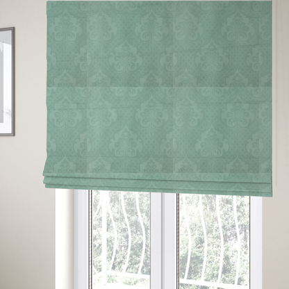 The fabric used to create these Roman blinds has a design that consists of large, ornate floral medallions and scrolling acanthus leaves woven in a shade very close to the background colour, creating a delicate, shimmering effect. A fine diagonal lattice grid fills the background between the motifs, and the material displays a clear woven texture throughout.