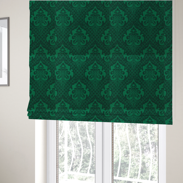 The fabric used to create these Roman blinds has a design that showcases large, ornate floral medallions and scrolling acanthus leaves in a vibrant green hue, set against a darker, forest green background. A fine diagonal lattice grid creates a diamond pattern in the spaces between the motifs, and the material displays a distinct woven texture that adds depth and classic character to the design.