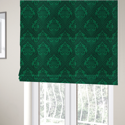 The fabric used to create these Roman blinds has a design that showcases large, ornate floral medallions and scrolling acanthus leaves in a vibrant green hue, set against a darker, forest green background. A fine diagonal lattice grid creates a diamond pattern in the spaces between the motifs, and the material displays a distinct woven texture that adds depth and classic character to the design.