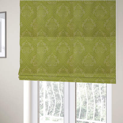 The fabric used to create these Roman blinds is a lime green damask pattern on a textured fabric. The design features large, ornate floral medallions with stylized acanthus leaves, arranged in a repeating grid.