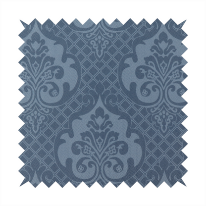 A dusty blue and steel grey damask pattern on a textured fabric. Large, ornate floral motifs with stylized acanthus leaves are arranged in a repeating grid. These medallions are a lighter, cool-toned blue-grey set against a darker navy-blue background.