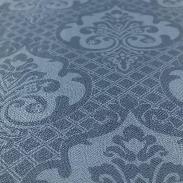 A dusty blue and steel grey damask pattern on a textured fabric. Large, ornate floral motifs with stylized acanthus leaves are arranged in a repeating grid. These medallions are a lighter, cool-toned blue-grey set against a darker navy-blue background.