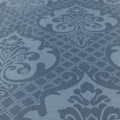 A dusty blue and steel grey damask pattern on a textured fabric. Large, ornate floral motifs with stylized acanthus leaves are arranged in a repeating grid. These medallions are a lighter, cool-toned blue-grey set against a darker navy-blue background.