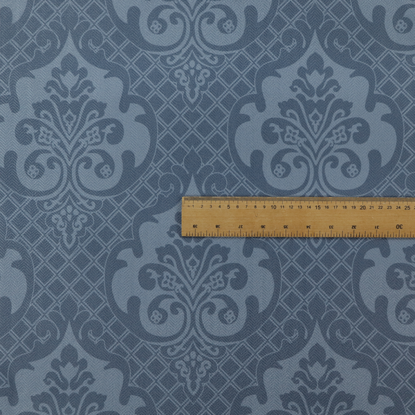A dusty blue and steel grey damask pattern on a textured fabric. Large, ornate floral motifs with stylized acanthus leaves are arranged in a repeating grid. These medallions are a lighter, cool-toned blue-grey set against a darker navy-blue background.