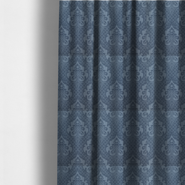 The fabric used to create these made-to-measure curtains has a dusty blue and steel grey damask pattern on a textured fabric. Large, ornate floral motifs with stylized acanthus leaves are arranged in a repeating grid. These medallions are a lighter, cool-toned blue-grey set against a darker navy-blue background.