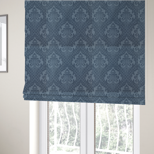 The fabric used to create these Roman blinds has a dusty blue and steel grey damask pattern on a textured fabric. Large, ornate floral motifs with stylized acanthus leaves are arranged in a repeating grid. These medallions are a lighter, cool-toned blue-grey set against a darker navy-blue background.