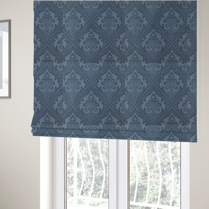 The fabric used to create these Roman blinds has a dusty blue and steel grey damask pattern on a textured fabric. Large, ornate floral motifs with stylized acanthus leaves are arranged in a repeating grid. These medallions are a lighter, cool-toned blue-grey set against a darker navy-blue background.