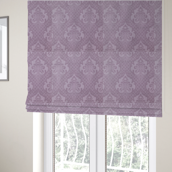 The fabric used to create these Roman blinds has a design that features large, ornate floral medallions and scrolling acanthus leaves in a light lavender shade, set against a slightly darker mauve background. A fine diagonal lattice grid fills the background between the motifs, and the material shows a clear woven texture that provides visual depth to the tonal design.