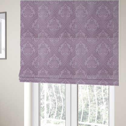 The fabric used to create these Roman blinds has a design that features large, ornate floral medallions and scrolling acanthus leaves in a light lavender shade, set against a slightly darker mauve background. A fine diagonal lattice grid fills the background between the motifs, and the material shows a clear woven texture that provides visual depth to the tonal design.