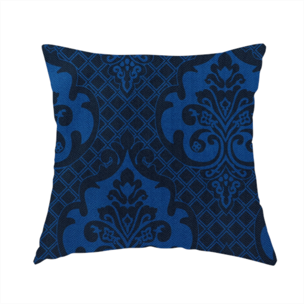 The fabric used to create this handmade cushion has a design that features large, ornate floral medallions and scrolling acanthus leaves in a bright royal blue shade, set against a deep navy background. A fine diagonal lattice grid fills the space between the motifs, and the material displays a clear woven texture that adds structural depth and a subtle sheen to the tonal blue design.