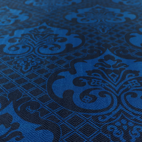The design features large, ornate floral medallions and scrolling acanthus leaves in a bright royal blue shade, set against a deep navy background. A fine diagonal lattice grid fills the space between the motifs, and the material displays a clear woven texture that adds structural depth and a subtle sheen to the tonal blue design.