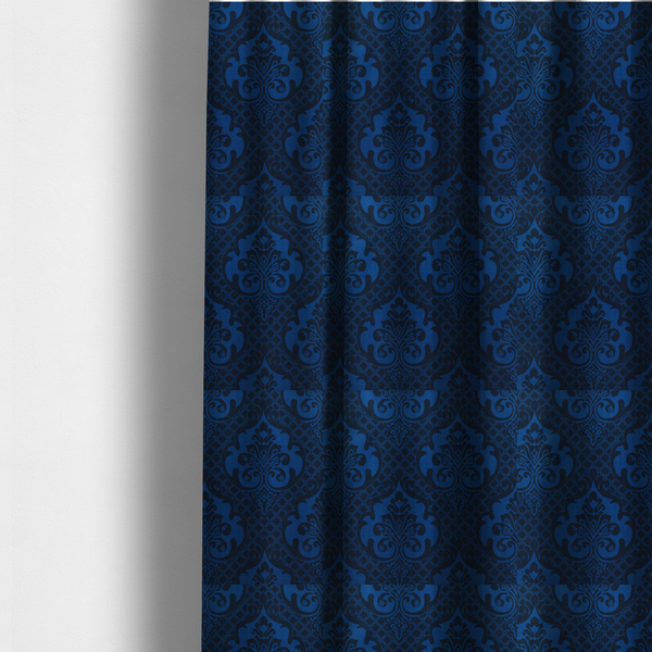 The fabric used to create these made-to-measure curtains has a design that features large, ornate floral medallions and scrolling acanthus leaves in a bright royal blue shade, set against a deep navy background. A fine diagonal lattice grid fills the space between the motifs, and the material displays a clear woven texture that adds structural depth and a subtle sheen to the tonal blue design.