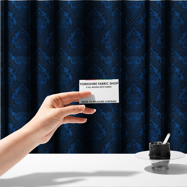 The fabric used to create these made-to-measure curtains has a design that features large, ornate floral medallions and scrolling acanthus leaves in a bright royal blue shade, set against a deep navy background. A fine diagonal lattice grid fills the space between the motifs, and the material displays a clear woven texture that adds structural depth and a subtle sheen to the tonal blue design.