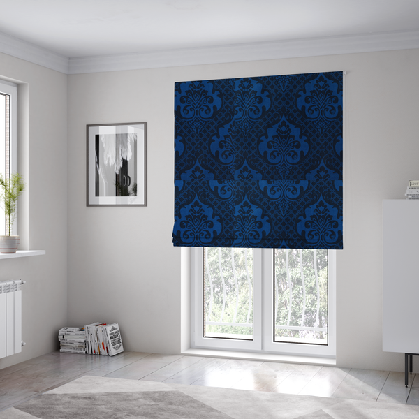 The fabric used to create these Roman blinds has a design that features large, ornate floral medallions and scrolling acanthus leaves in a bright royal blue shade, set against a deep navy background. A fine diagonal lattice grid fills the space between the motifs, and the material displays a clear woven texture that adds structural depth and a subtle sheen to the tonal blue design.
