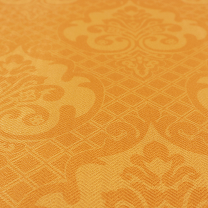 An orange damask pattern on a textured fabric. Large, ornate floral motifs and scrolling acanthus leaves are arranged in a repeating grid. These motifs are rendered in a soft peach shade against a more saturated, vibrant orange background.