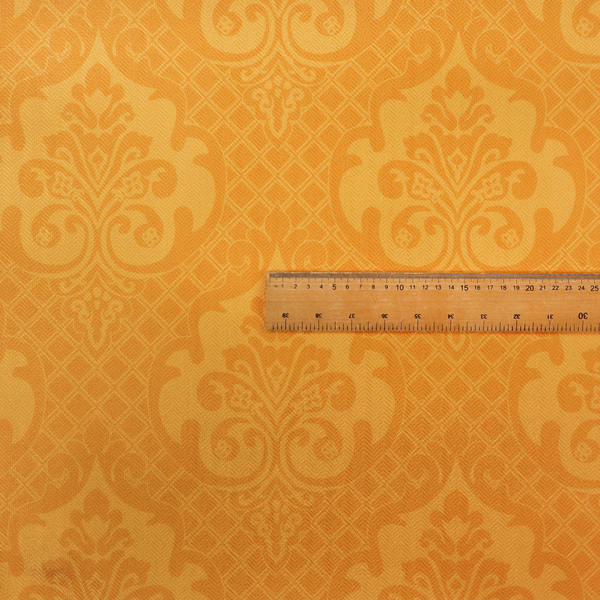 An orange damask pattern on a textured fabric. Large, ornate floral motifs and scrolling acanthus leaves are arranged in a repeating grid. These motifs are rendered in a soft peach shade against a more saturated, vibrant orange background.