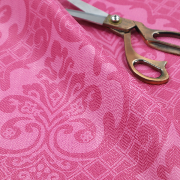 The design features large, ornate floral medallions and scrolling acanthus leaves in a lighter pink shade, set against a saturated magenta-rose background. A fine diagonal lattice grid fills the background between the motifs, and the material shows a clear woven texture that provides visual depth to the traditional design.