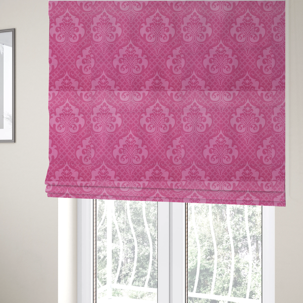 The fabric used to create these Roman blinds has a design that features large, ornate floral medallions and scrolling acanthus leaves in a lighter pink shade, set against a saturated magenta-rose background. A fine diagonal lattice grid fills the background between the motifs, and the material shows a clear woven texture that provides visual depth to the traditional design.